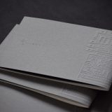 Several dark grey brochures lie stacked on top of each other. LuxConnect" is embossed on the cover.