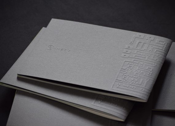 Several dark grey brochures lie stacked on top of each other. LuxConnect" is embossed on the cover.