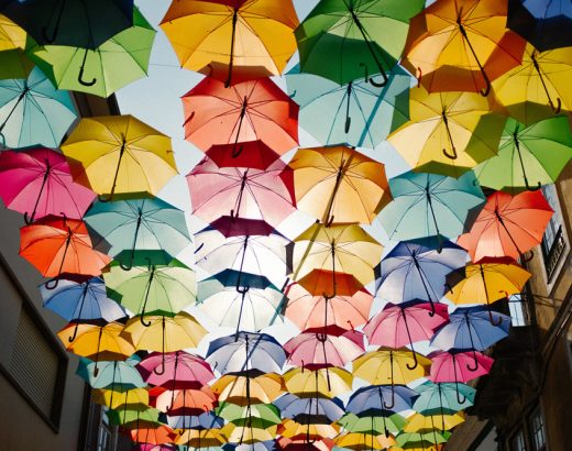 Entlang einer gesamten Straße sind hoch an den Gebäuden bunte Regenschirme in Sechserreihen an Schnürren befestigt.