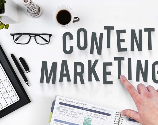 Das Bild gehört zum Beitrag »Content-Strategie« und zeigt verschiedene Büroartikel, die auf einem Schreibtisch liegen. Eine Hand zeigt auf das Wort "Content Marketing", das in Großbuchstaben geschrieben im Fokus des Bildes steht.