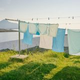 Greenwashing: Eine Wäscheleine mit pastellfarbener Wäsche bedeckt das Bild zu 3/4. Im Hintergrund sind Berge zu sehen.