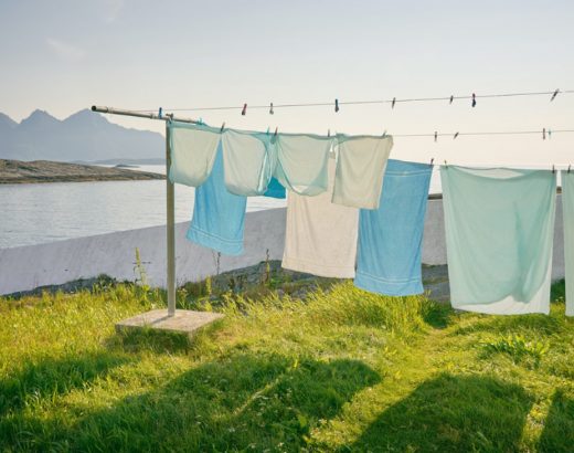 Greenwashing: Eine Wäscheleine mit pastellfarbener Wäsche bedeckt das Bild zu 3/4. Im Hintergrund sind Berge zu sehen.