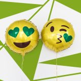 Es sind zwei Luftballon mit Emoji-Motiven. Der linke Luftballon ist rund, gelb und das Emoji hat einen offenes lachen. Die Augen sind zwei grüne Herzen. Der rechte Luftballon hat ein Kussmund geformt woraus ein grünes Herz kommt. Die Augen zwinkern einem zu. Diese Smiley werden im Emoji-Marketing eingesetzt.