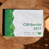 Eine Broschüre in verschiedenen Grüntönen und in Weiß liegt auf einem Holz-Beistelltisch. Der Titel der Broschüre lautet »CSR-Bericht 2017«.